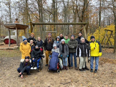 Das Foto zeigt 16 Jugendliche und junge Erwachsene. Alle sind warm angezogen. Im Hintergrund ist ein Waldspielplatz zu sehen.