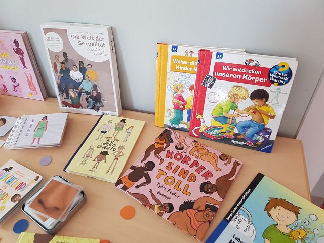 Auf dem Bild sind mehrere Kinderbücher zu verschiedenen Themen abgebildet. Die Bücher behandeln Themen wie Sexualität, den menschlichen Körper und Vielfalt. Einige Buchcover zeigen Illustrationen von Menschen in verschiedenen Aktivitäten und Lebenssituationen. Die Bücher sind auf einem Holztisch ausgebreitet.